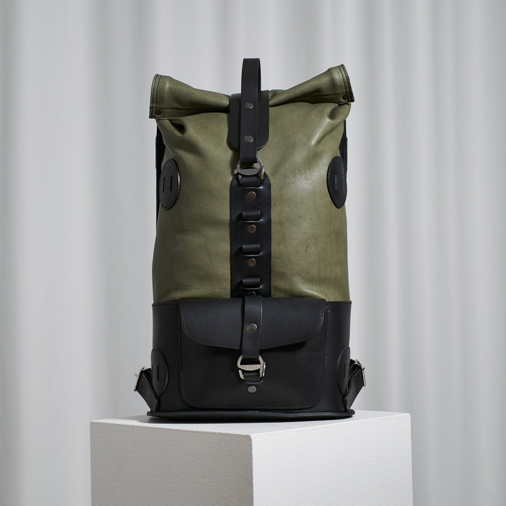 Sage and Black Fold Top leather backpack – front view on a white plinth, sage green top with black base